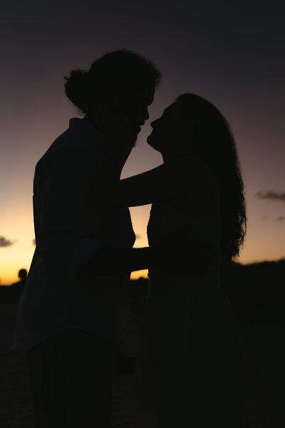 Romantic silhouette of an engaged couple sharing a sunset kiss