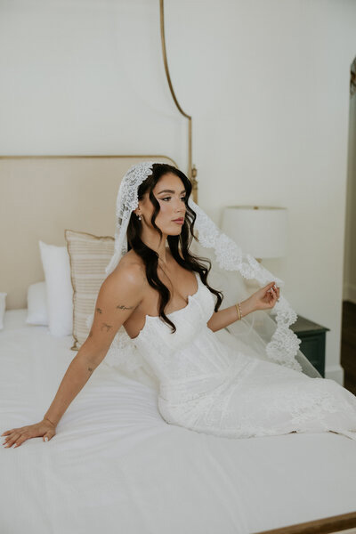 Bride sitting on a bed while getting ready on her wedding morning
