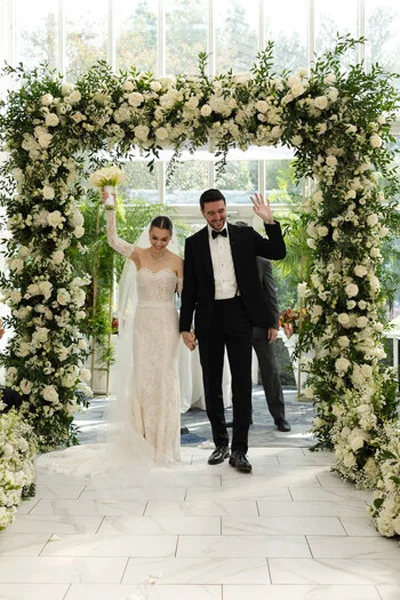 Bride and groom making their grand entrance beneath a floral wedding arch